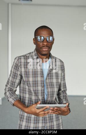Porträt eines afrikanischen jungen Mannes in einer Brille, der die Kamera anschaut Bei Verwendung eines digitalen Tablets Stockfoto