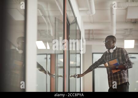 Afrikanischer junger Mann in lässiger Kleidung öffnet die Tür von Sitzungssaal kommt er bei der Sitzung Stockfoto