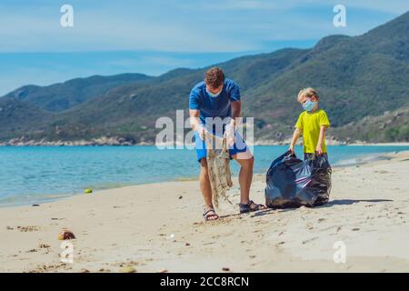 Volunteers blaue Gesichtsmaske Paradies Strand Sand lazur Meer. Vater Sohn abholen Müll in schwarzen Beutel. Problem verschüttete Müll Müll Müll Planeten Verschmutzung Stockfoto