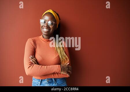 Portrait von African glückliche Frau mit stilvollen Frisur und in Brillen lächeln vor der Kamera, während sie vor dem braunen Hintergrund stehen Stockfoto