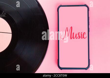 Vinyl-Disc und Smartphone auf einem rosa Hintergrund. Flach liegend. Platz kopieren und Mock-up. Das Konzept der Evolution der Musiktechnologie. Stockfoto