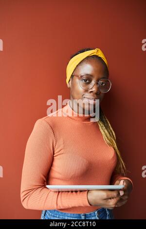 Portrait der afrikanischen jungen Frau mit schönen Frisur hält digital Tablet und Blick auf die Kamera isoliert auf braunem Hintergrund Stockfoto