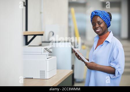 Portrait einer afrikanischen Designerin, die beim Making die Kamera anlächelt Kopieren auf Kopiergerät im Büro Stockfoto