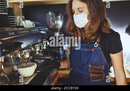 Barista trägt Gesichtsschutz Maske und medizinische Latex schwarze Handschuhe, Vorbereitung Kaffee trinken mit Espresso-Maschine im Café Café. Stockfoto