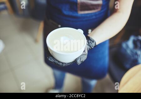 Barista trägt medizinische Latexhandschuhe, macht Cappuccino, Barkeeper bereitet Kaffee trinken. Verschwommenes Bild, selektiver Fokus Stockfoto