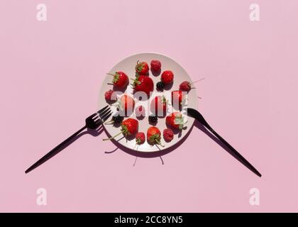 Frische Beeren, Erdbeeren, Himbeeren, Brombeeren in rosa Keramikplatte auf rosa Hintergrund. Vegetarische oder fruitarische Diät-Konzept. Stockfoto