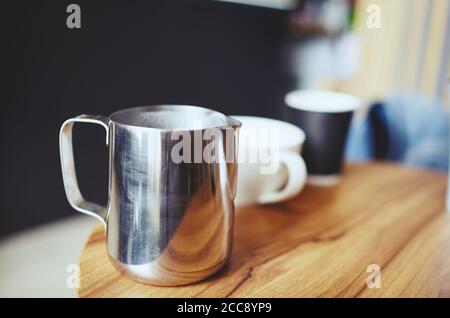 Verschwommenes Bild von Milchkännchen und einer Tasse Kaffee auf einem Holztisch im Café. Kaffeepause Stockfoto