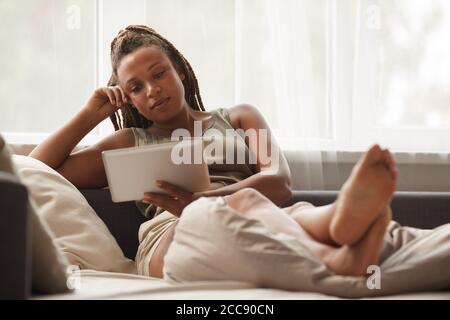 Junge Frau, die Film auf dem digitalen Tablet beim Entspannen auf Sofa am Wochenende Stockfoto
