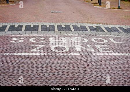 Die Worte "Schulzone" witten in weißer Farbe auf einer Backsteinstraße in wolle, Niederlande, um die Fahrer zu einer Geschwindigkeitsreduzierung zu ermutigen Stockfoto