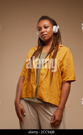 Portrait der Mode Frau in Kopfhörer und stilvolle Kleidung hören Zu Musik, die auf braunem Hintergrund isoliert ist Stockfoto
