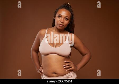 Portrait der afrikanischen jungen Frau mit plump Formen Blick auf Kamera vor dem braunen Hintergrund Stockfoto
