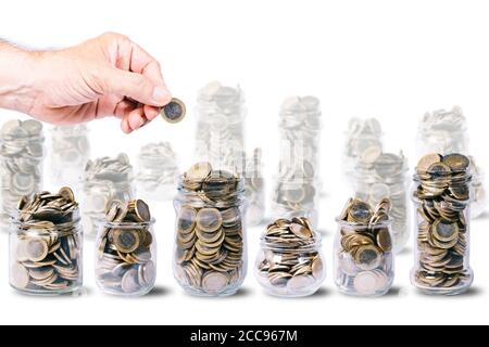 Männliche Hand mit einer Euro-Münze über mehreren Gläsern voller Euro-Münzen, andere Gläser unscharf, auf weißem Hintergrund mit Kopierraum Stockfoto