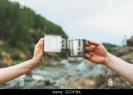 Junge Paar Reisende mit Metallbechern auf Berg Fluss Hintergrund. Lokaler Tourismus, Wochenendausflug, Mock Up Stockfoto