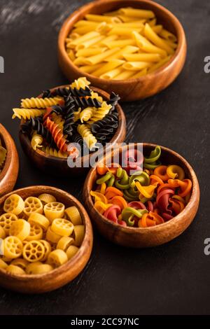 Selektive Fokussierung verschiedener roher italienischer Pasta in Holzschalen Auf schwarzem Hintergrund Stockfoto