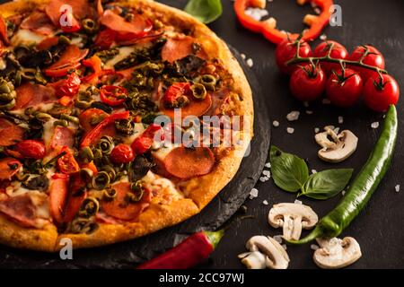 Leckere italienische Pizza mit Salami in der Nähe von Gemüse auf schwarzem Hintergrund Stockfoto