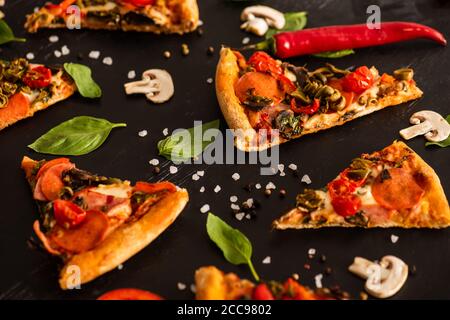 Selektive Fokus der köstlichen italienischen Pizza Scheiben mit Salami in der Nähe Gemüse auf schwarzem Hintergrund Stockfoto
