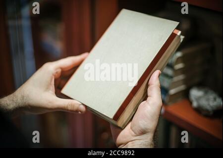 Neugieriger Mann, der Buch in seiner Bibliothek zu Hause wählt. Nahaufnahme Stockfoto