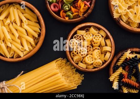 Draufsicht auf verschiedene bunte italienische Pasta in Holzschüsseln Auf schwarzem Hintergrund Stockfoto