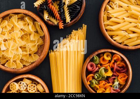 Draufsicht auf verschiedene bunte italienische Pasta in Holzschüsseln Auf schwarzem Hintergrund Stockfoto