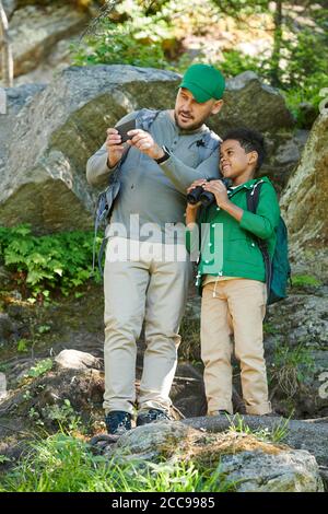 Mann mit dem Jungen, der auf den Felsen steht und nimmt Bild der schönen Natur auf dem Handy Stockfoto