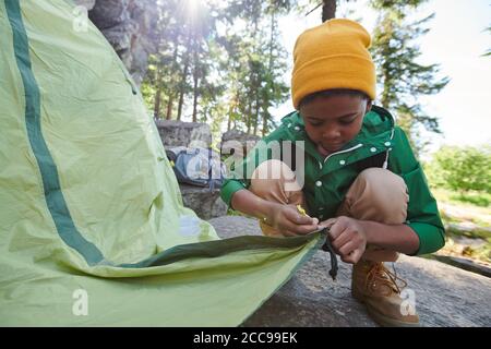 Afrikanischer kleiner Junge, der während des Campens in das Zelt aufstellend Die Natur Stockfoto