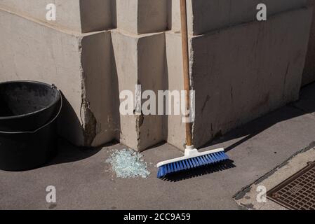 Ein Stapel zerbrochenes Glas neben einem blauen Besen und einem schwarzen Eimer auf dem Boden an einer Straßenecke in Wien, Österreich Stockfoto