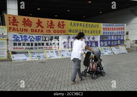 Frau mit Kinderwagen, die an politischen Spruchbändern zur Unterstützung von Falun Gong vorbeigeht. Tung Chung, Lantau Island, Hongkong. Stockfoto