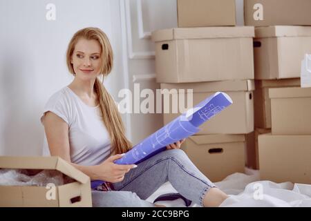 Mädchen sitzt zwischen Boxen macht Marken auf dem Plan der Wohnung Stockfoto