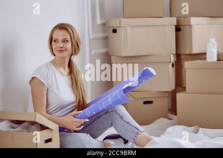 Mädchen sitzt zwischen Boxen macht Marken auf dem Plan der Wohnung Stockfoto