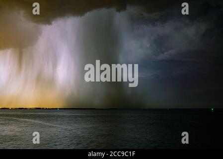 Dramatisches Naturbild eines Gewitters mit ausgeprägter Regen- und Hagelwelle über einem See. Nachtbild. Stockfoto