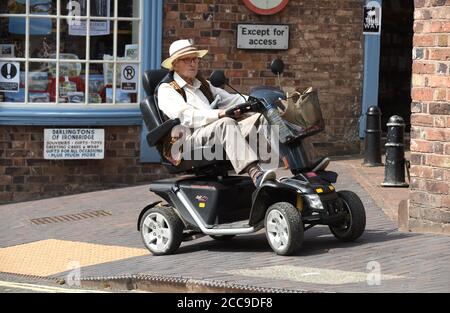 Älterer Mann, der seinen Stolz Colt Executive Mobility Scooter unterwegs fährt, Großbritannien, Großbritannien Stockfoto