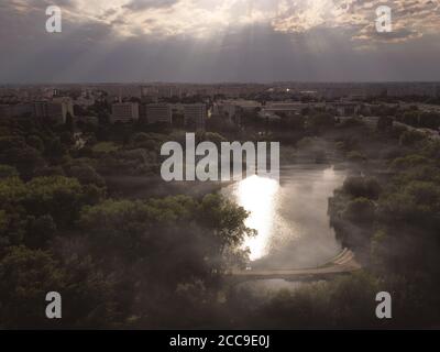 Wunderschöner Blick auf den Park, der in Sonnenstrahlen gebadet ist, mit wenig Nebel über einem Teich. Drohne, Luftaufnahme Stockfoto