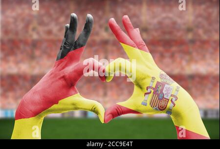 Die Hände eines Menschen bilden ein Herz mit den Flaggen Deutschlands Und Spanien - Liebe zum Fußball-Konzept Stockfoto