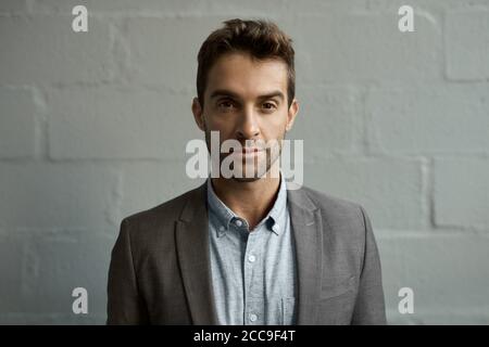 Fokussierter junger Geschäftsmann, der vor einer Backsteinmauer steht Stockfoto