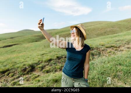 Junge Frau, die im Sommer ein Selfie auf einer Bergwiese gemacht hat Stockfoto