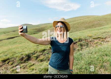 Junge Frau, die im Sommer ein Selfie auf einer Bergwiese gemacht hat Stockfoto