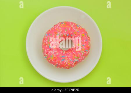Ein rosa glasierte Donut auf weißem Teller auf grünem Hintergrund. Stockfoto