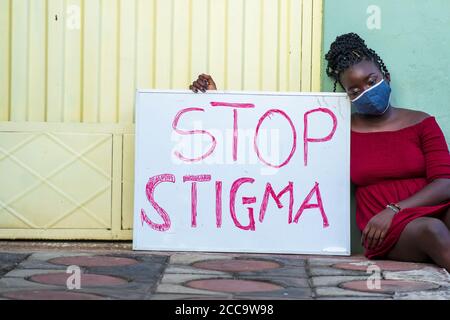 Junge schwarze Hündin mit einer medizinischen Maske, die ein Brett hält Mit Text 'Stop Stigma' Stockfoto