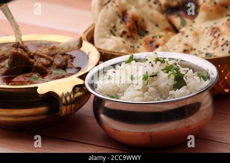 Hammelcurry serviert mit Naan oder Brot und Jeera-Reis auf Holzhintergrund. Stockfoto