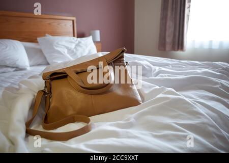 Foto einer Handtasche auf einem ungefertigten Bett in einem Hotelzimmer. Stockfoto