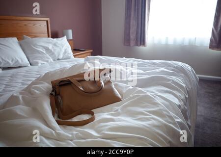 Foto einer Handtasche auf einem ungefertigten Bett in einem Hotelzimmer. Stockfoto