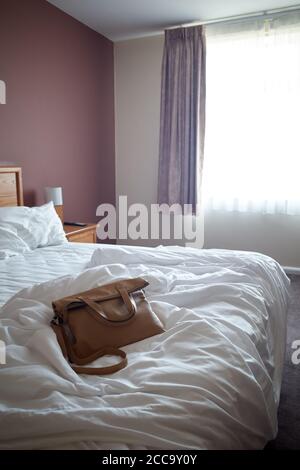 Foto einer Handtasche auf einem ungefertigten Bett in einem Hotelzimmer. Stockfoto