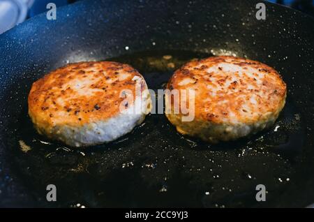 Zwei runde Koteletts aus Rindfleisch werden darin gebraten Eine Pfanne und Öl Stockfoto