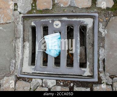 Eine Einweg-Gesichtsmaske auf einem Abflussdeckel in Shrewsbury, Shropshire. Stockfoto