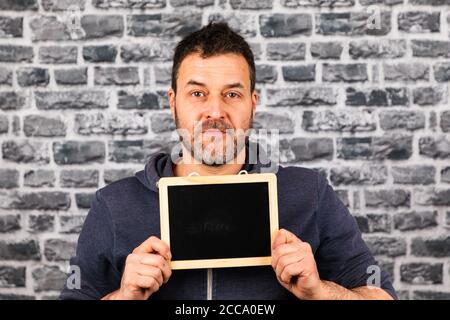 Kaukasischer Mann, der eine kleine Tafel in den Händen hält Vorderseite einer grauen Kopfsteinpflasterwand Stockfoto