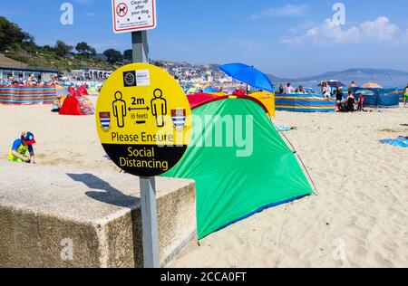 Am Strand anmelden: Bitte sorgen Sie für soziale Distanzierung, bei Lyme Regis, einem beliebten Badeort an der Jurassic Coast in Dorset, SW England Stockfoto