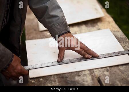 Ältere ältere Tischler mit einem Lineal eine Linie zu ziehen Auf einem Brett Stockfoto