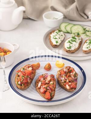 Frische mediterrane Bruschetta mit Tomate, Olivenöl, Petersilie und roter Zwiebel auf einem Teller auf hellem Hintergrund. Stockfoto