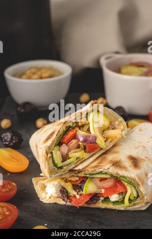 Vegane Tortilla Wrap gefüllt mit Hummus und frischem Gemüse auf dunklem Hintergrund platziert. Bereit zum Essen. Stockfoto