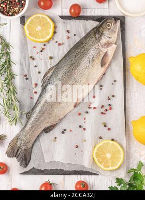 Frische, rohe Forelle mit Rosmarin, Kirschtomate, Petersilie, Pfeffer, Salz und Zitrone. Gesundes mediterranes Essen und Diät-Konzept, Draufsicht, Flat Lay. Stockfoto